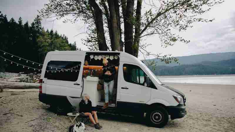 A couple with their dog relax by a camper van on a serene beach, embracing outdoor lifestyle., tags: hire - pexel