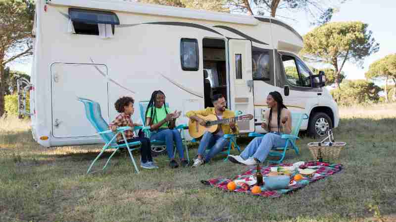 A family relaxing outdoors with a picnic and guitar by their camper, enjoying a sunny summer day in Portugal., tags: road holiday - pexel
